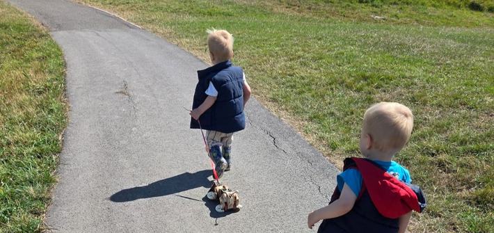 two toddlers walking through a park with pull-along dog toys