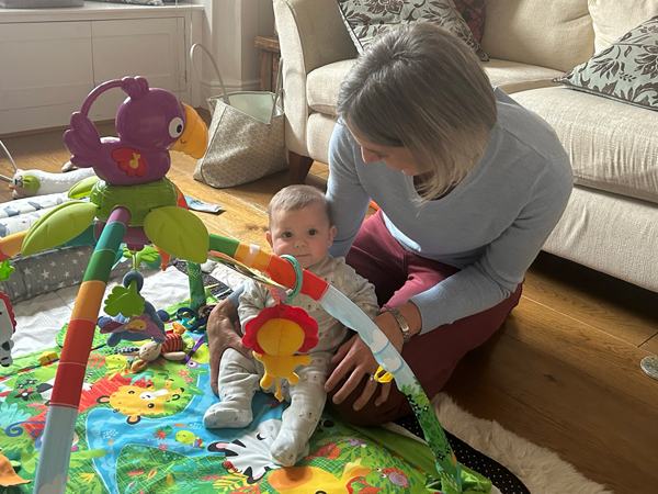 a woman helping a baby sit up on a play mat