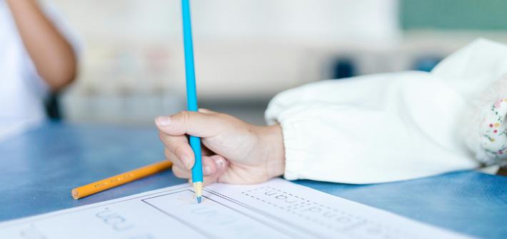 close up of a child's hand using a blue pencil to fill in a worksheet
