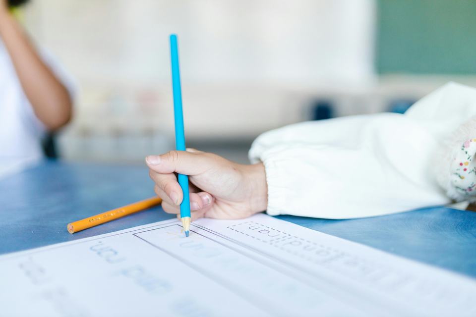 close up of a child's hand using a blue pencil to fill in a worksheet