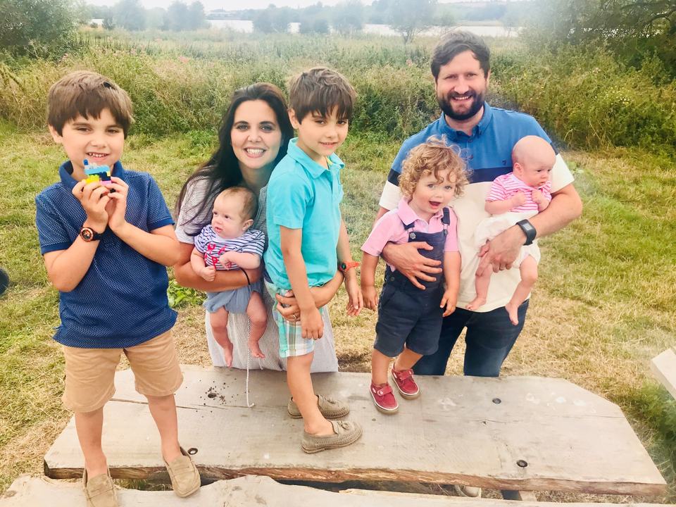 a mother and father with their twin boys, a toddler and twin babies in a park