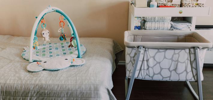 A baby crib sits next to a bed with a baby play frame sitting on it
