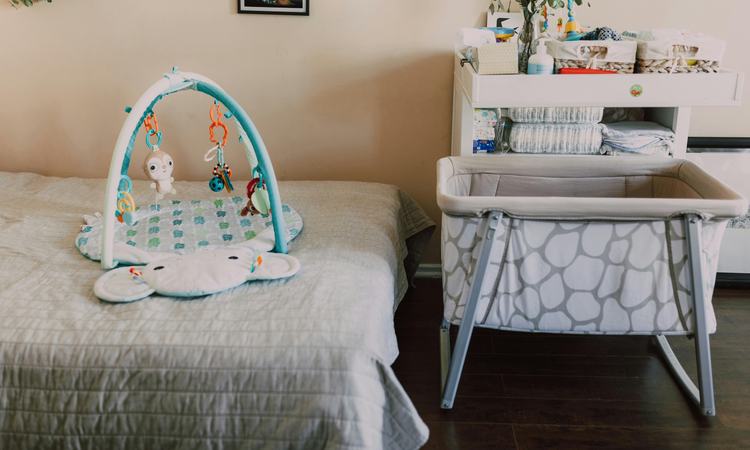 A baby crib sits next to a bed with a baby play frame sitting on it