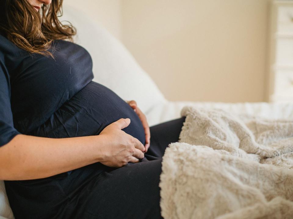 pregnant woman sitting on a bed holding her tummy