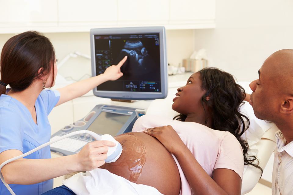 a black pregnant woman having a sonography with her partner beside her