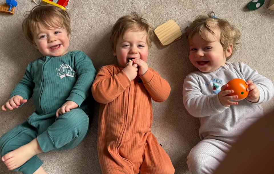 three baby triplets smiling and lying on the carpet floor