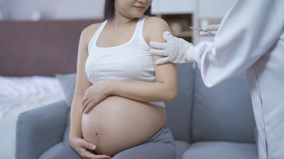 a pregnant Asian woman having an injection into the arm by a doctor