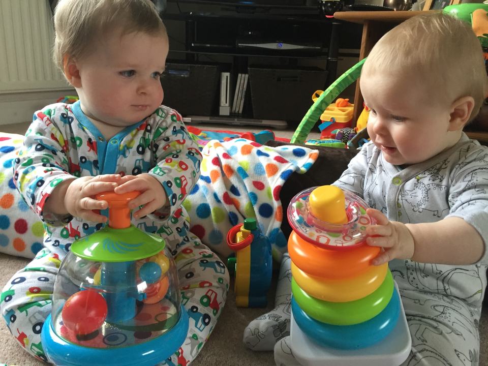 two twin babies playing with a spinning top and stacking rings