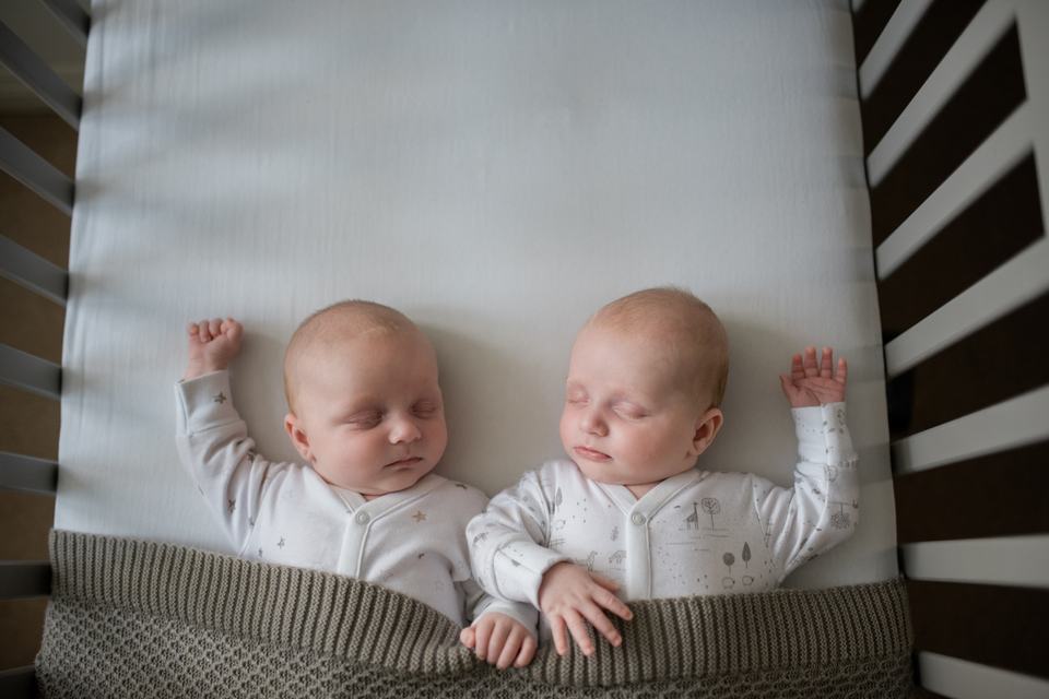 two twin babies sleeping next to each other in a cot
