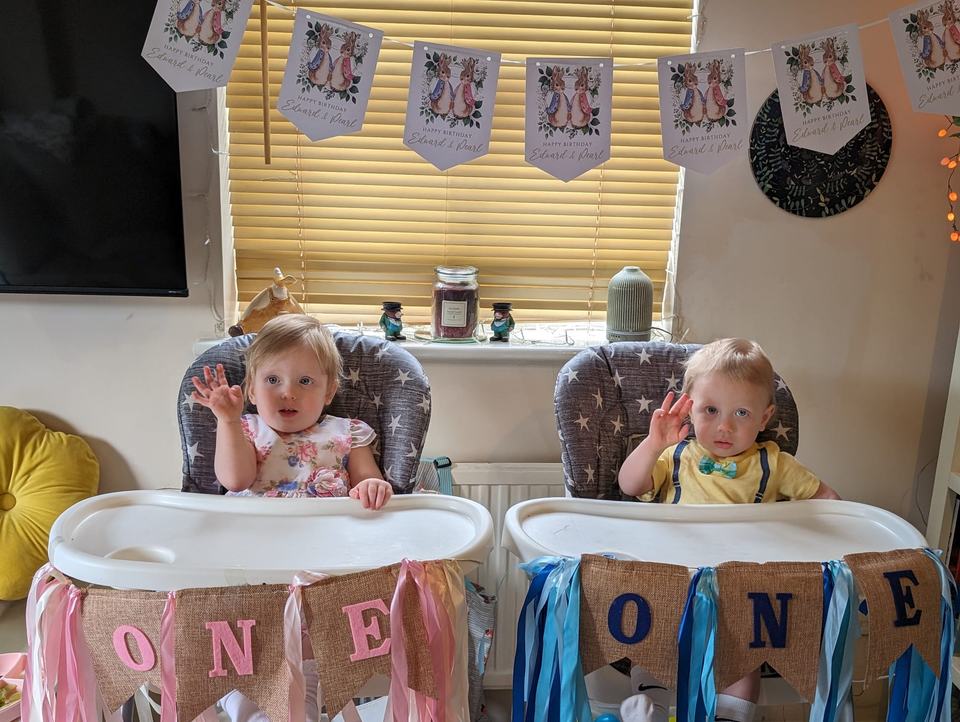two twin babies sat in their highchairs on their first birthday