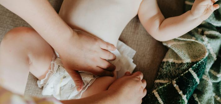 A close-up overhead view of a pair of hands putting a nappy on a baby