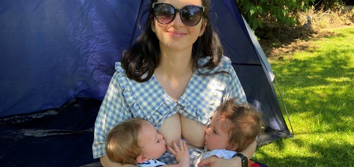 a mother tandem breastfeeding twins in a tent in a park