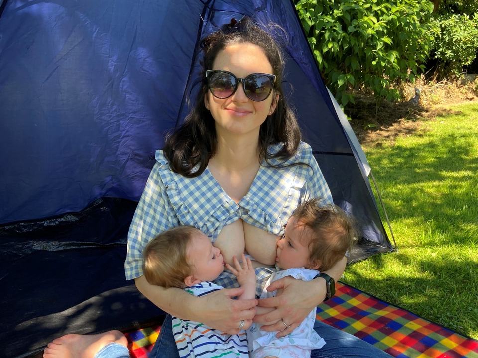 a mother tandem breastfeeding twins in a tent in a park