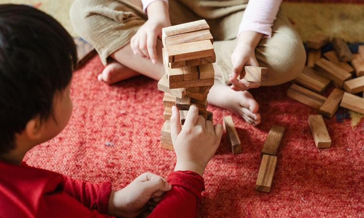 A close-up image of two children sat on the floor playing a game of Jenga