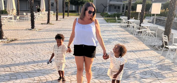 a mother holding her twin children's hands walking through a holiday resort