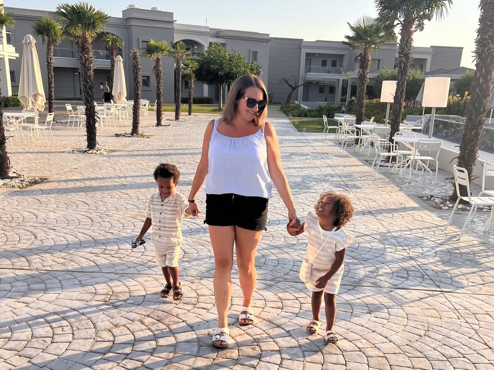 a mother holding her twin children's hands walking through a holiday resort