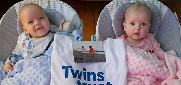 Twin babies lie in cribs with a Twins Trust bag between them