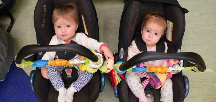 Twin babies sit in car seats placed next to each other