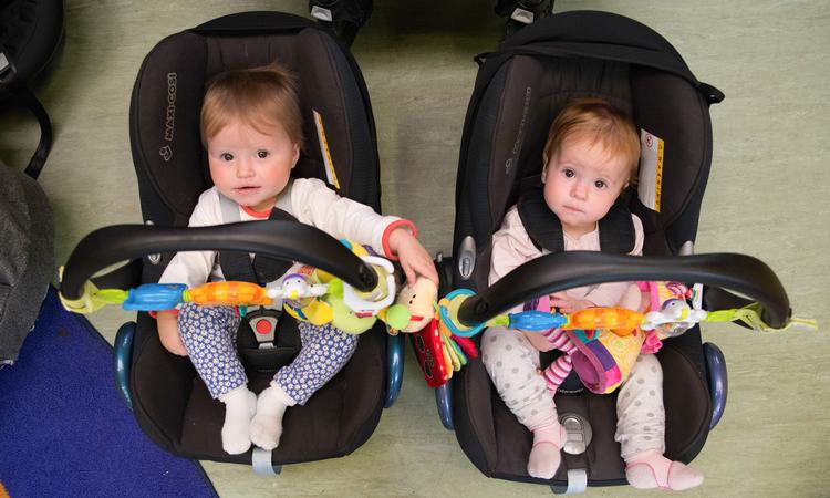 Twin babies sit in car seats placed next to each other