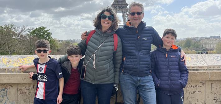 a family of five smiling on a bridge in front of the Eiffel tower