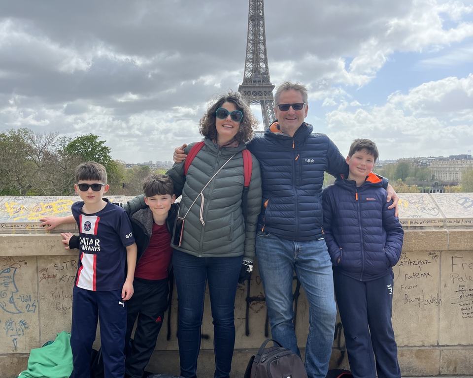 a family of five smiling on a bridge in front of the Eiffel tower