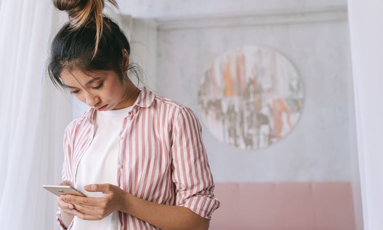 A woman stands looking down at her smartphone