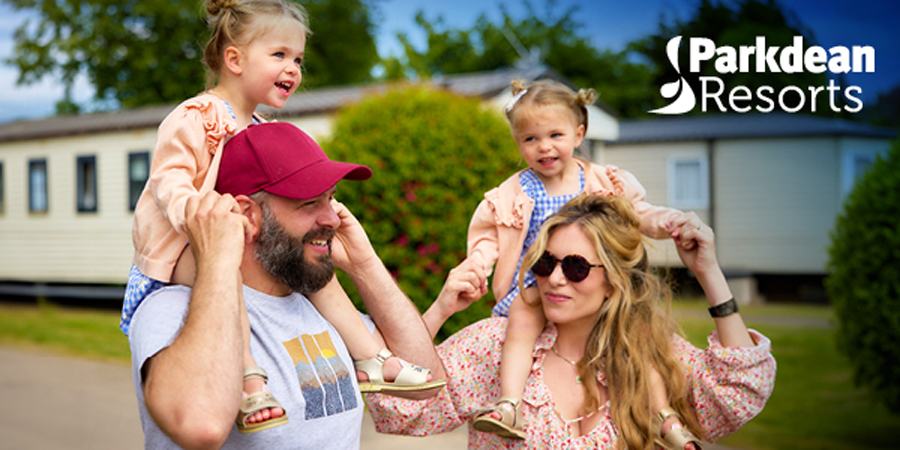 A man and a woman walk together through a caravan park with twin girls on their shoulders