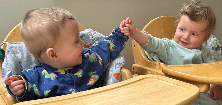 Twin babies sit in high chair high fiving each other