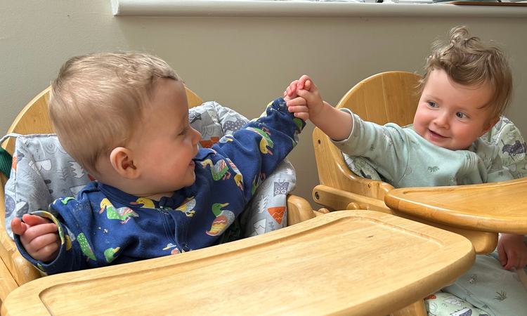 Twin babies sit in high chair high fiving each other
