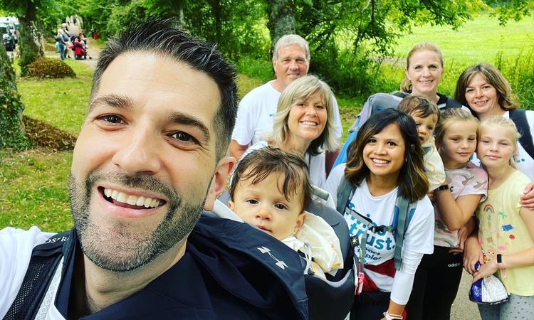 A man takes a selfie with a group of people gathered behind him