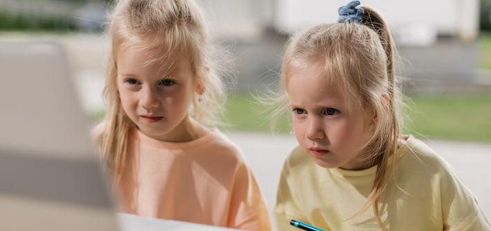 Twin girls sit concentrating on a laptop screen