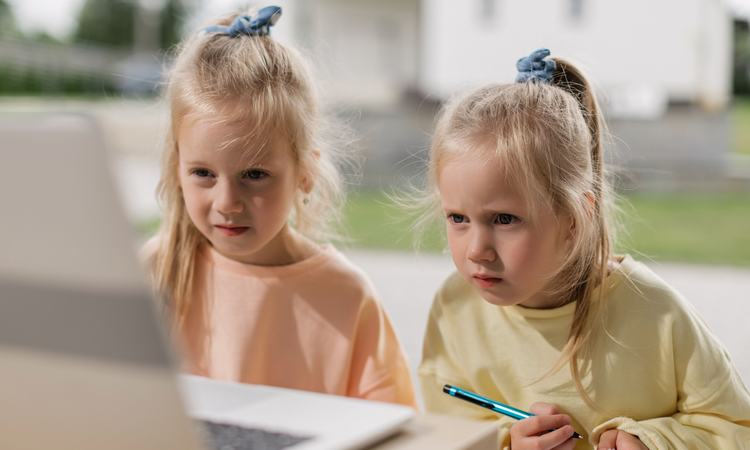 Twin girls sit concentrating on a laptop screen