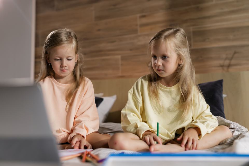 twin girls sat on a bed learning at home
