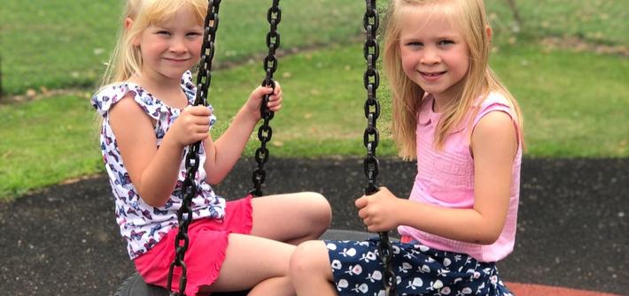 twin girls sitting on a tyre swing at the park
