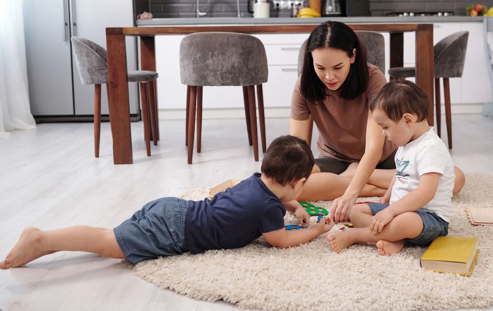 a mother playing with her twin boys on a rug in the dining room
