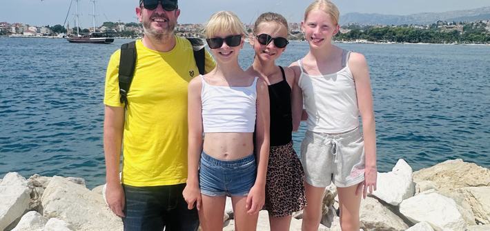 a father standing with his three daughters by a lake