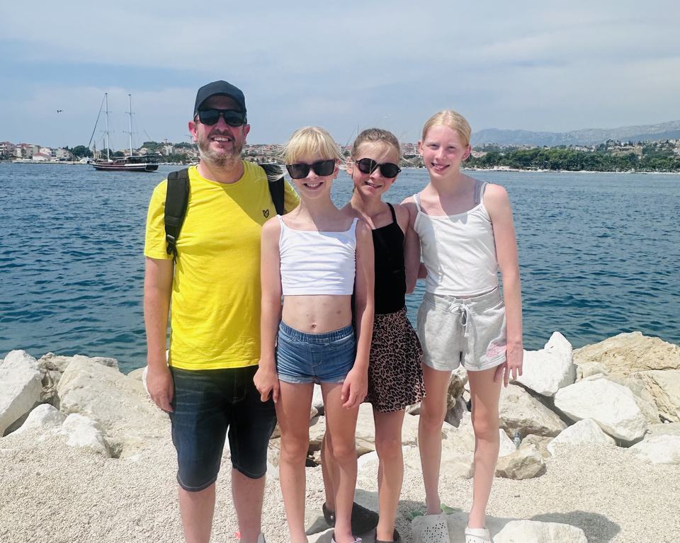a father standing with his three daughters by a lake