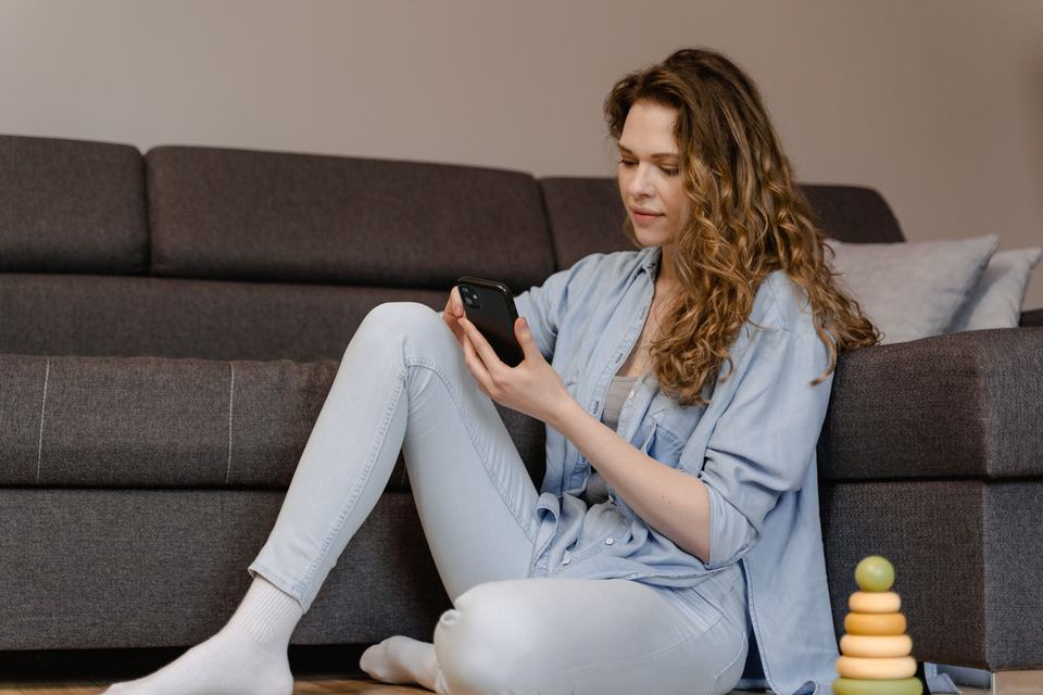 a woman sat on floor of living room texting on her smartphone