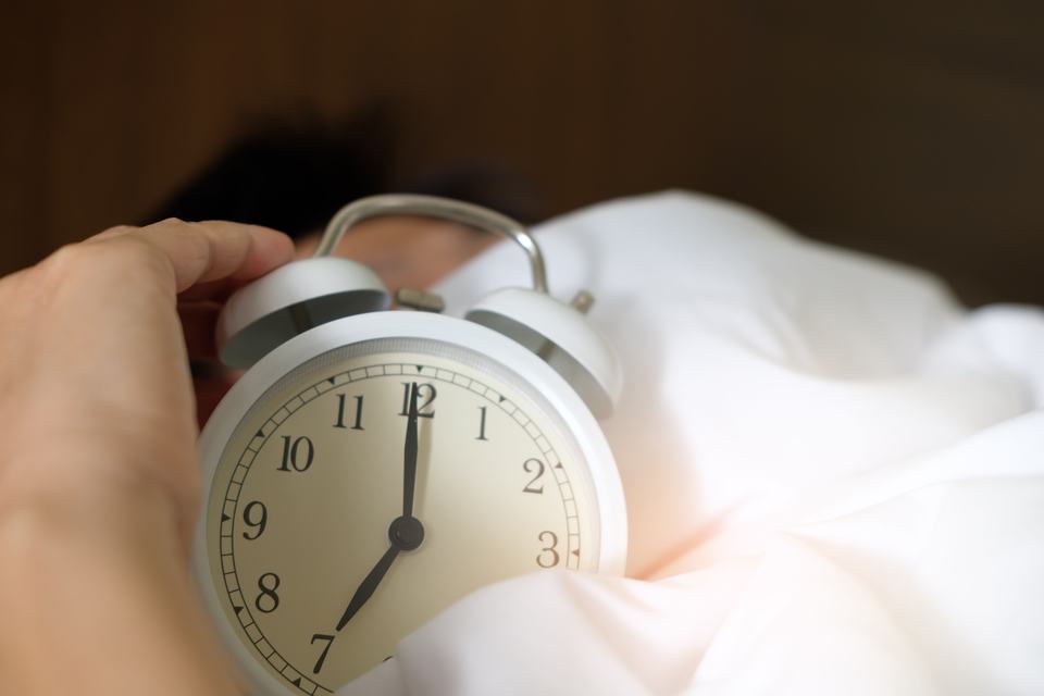 A close-up of a hand reaching for a ringing alarm clock, symbolising waking up in the morning