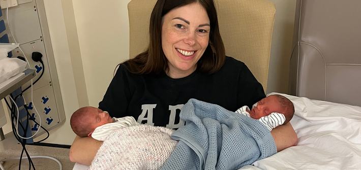 A woman sits in a hospital chair cradling two newborn babies