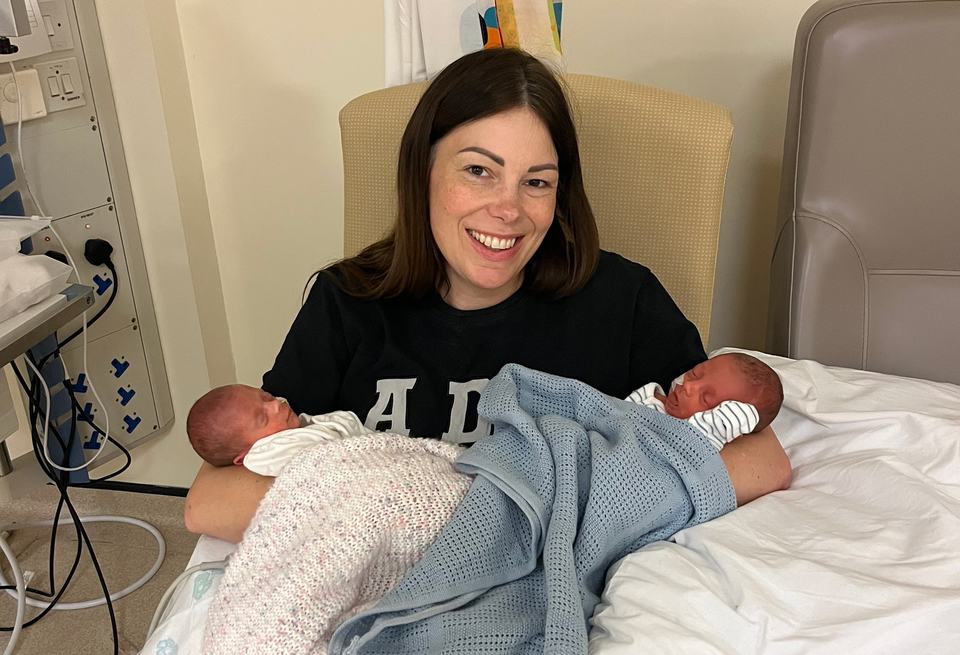 A woman sits in a hospital chair cradling two newborn babies