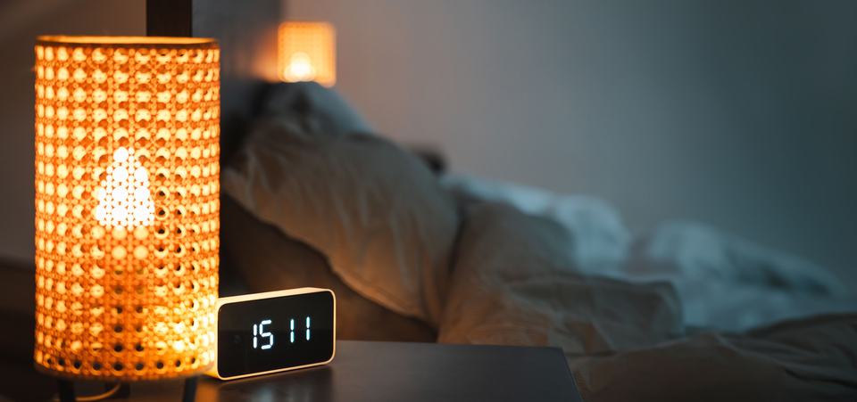 a clock and bedside lamp on a bedside table in a calm bedroom