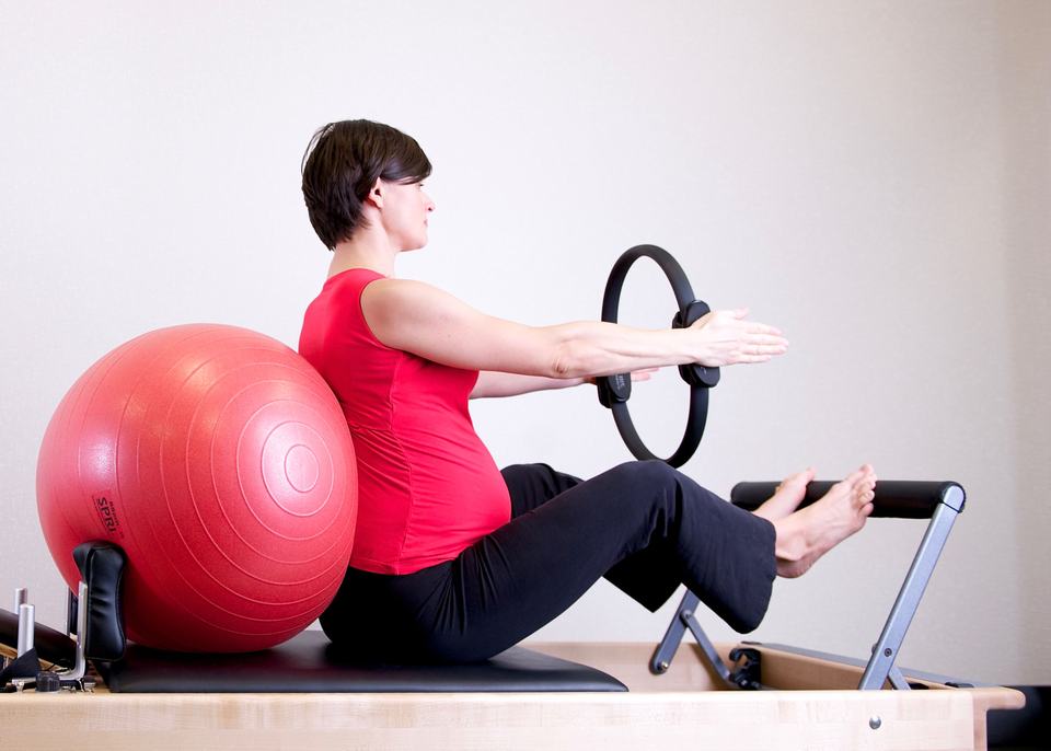 A pregnant woman practicing Pilates using a fitness ring and exercise ball in a gym setting