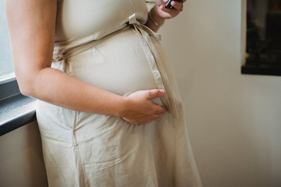 a pregnant woman holding her belly while using a smartphone at home