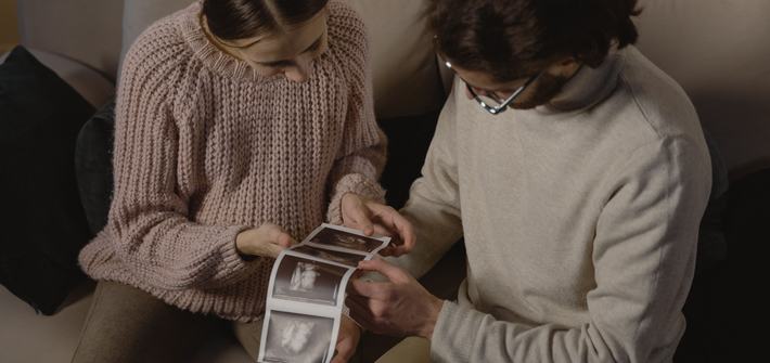 A couple sits indoors, joyfully examining ultrasound images, celebrating an upcoming additions to their family.