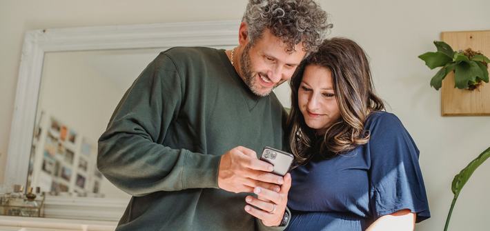 Pregnant couple joyfully viewing a mobile phone in cosy home setting.