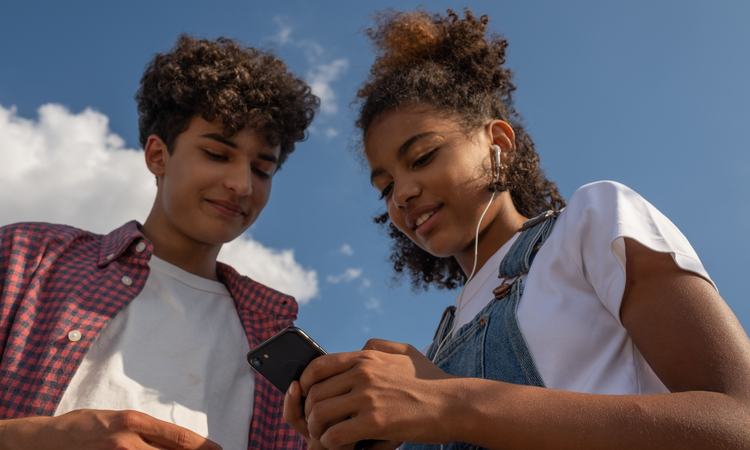Two teenagers enjoy music together outdoors using a smartphone and earphones