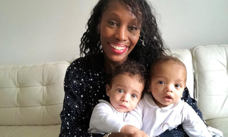 A black woman smiles at the camera holding twin babies on her lap