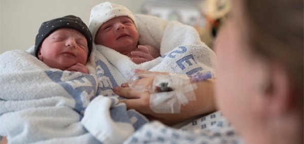 newborn twin babies wrapped in towels held by their mother in hospital