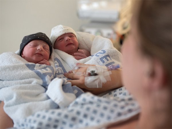 newborn twin babies wrapped in towels held by their mother in hospital